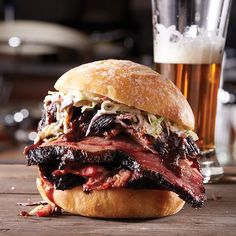 a roast beef sandwich on a wooden table next to a glass of beer