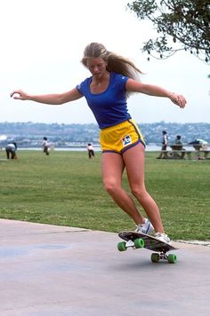 a woman riding a skateboard on top of a cement walkway next to a park