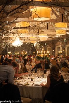 a large group of people sitting at tables in a room with chandeliers hanging from the ceiling