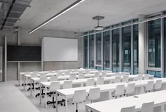 an empty classroom with white desks and chairs in front of a projection screen on the wall