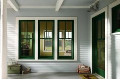 the front porch is painted white and has green trim on the windows, along with two suitcases