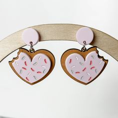 These irresistible sugar cookies with pink frosting make great Valentine's Day earrings! Crafted from wood and acrylic, each earring features a delightful bite and sprinkles on top. Perfect for cookie enthusiasts or a romantic touch on Valentine's Day, these earrings measure approximately 2" in length and 1.5" in width. Sweet Heart Earrings For Valentine's Day, Cookie Heart, Pink Frosting, Wood And Acrylic, Valentines Day Cookies, Heart Dangle Earrings, Small Heart, A Romantic, Sugar Cookies