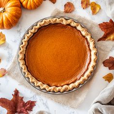 a pie sitting on top of a table next to pumpkins and other autumn leaves