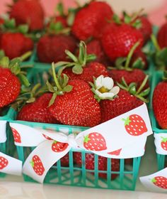 there are many strawberries in baskets with white ribbons on the sides and one is red