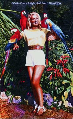 a woman with two parrots on her shoulders in front of flowers and plants,