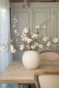 a white vase filled with flowers sitting on top of a wooden table next to a chair