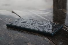 a tablet computer sitting on top of a wooden table covered in rain drops and water