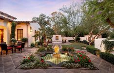 an outdoor patio with a fountain surrounded by flowers and greenery