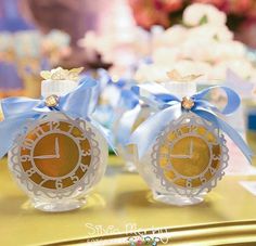 two small glass clocks with blue bows on them sitting on top of a gold table