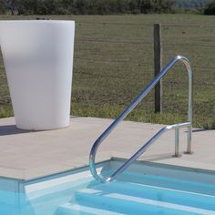 an empty swimming pool next to a metal hand rail with a large white cup on it