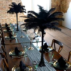 the table is set with black place settings and tall centerpieces that have feathers on them