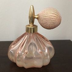 a pink glass perfume bottle with a gold top on a wooden table next to a white wall