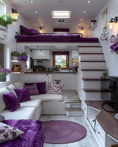 a living room filled with lots of furniture and purple pillows on top of white couches