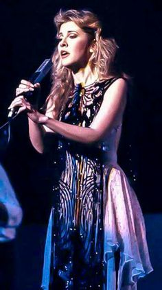 a woman with long hair holding a microphone in her hand and singing into the microphone