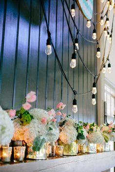 a mantel with candles, flowers and lights hanging from the ceiling in front of it