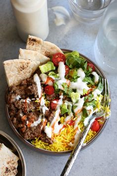 a plate full of food with pita bread, salad and milk on the side