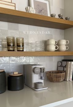 a kitchen counter with coffee cups and other items on the shelf above it that says wednesday