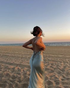 a woman standing on top of a sandy beach next to the ocean with her back turned