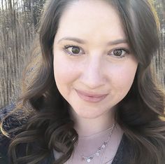 a close up of a person wearing a necklace and smiling at the camera with trees in the background