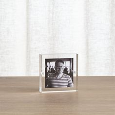 a photo frame sitting on top of a wooden table next to a window with curtains in the background