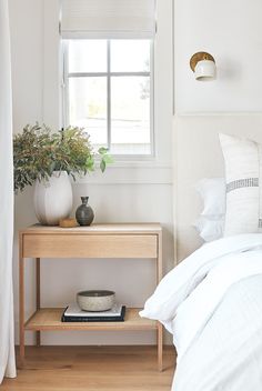 a bedroom with a bed, nightstand and plant on the side table in front of the window