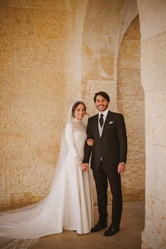 a bride and groom standing in front of a stone wall