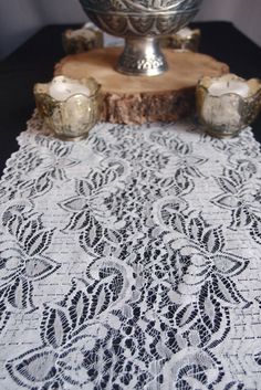 an ornate lace table runner with candles on it and a silver bowl in the background