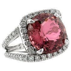 A stunning and important new ring by Eytan Brandes features a two-piece, cushion-shaped halo of diamonds around a gorgeous Brazilian pink tourmaline. The tourmaline is 11.7mm in diameter and weighs 6.08 carats. It boasts a tricky mixed cut -- brilliant cut, like a diamond, on the crown, and Portuguese cut on the pavilion. It is a completely natural stone -- no dyes, no heat treatments. The 54 surrounding diamonds are set in modern U-prongs to form strong, sparkly lines around the center stone and alone the split shoulders. These diamonds are full cut, earth-mined and untreated, with a total weight of 0.81 carats. Our supplier rates these stones G-H color and VS2-SI1 clarity; Eytan agrees with this assessment. The face of the ring is 14mm wide and 14.5mm tall. The split shoulders taper to a Platinum Halo Ring, Pink Tourmaline Engagement Ring, Dress Reference, Tourmaline Engagement Ring, Baguette Engagement Ring, Contemporary Engagement Rings, The Pavilion, Bad Kids, Platinum Diamond Rings