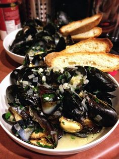 mussels and bread sit on a table next to each other