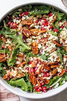 a salad with pecans, feta cheese and pomegranates in a white bowl