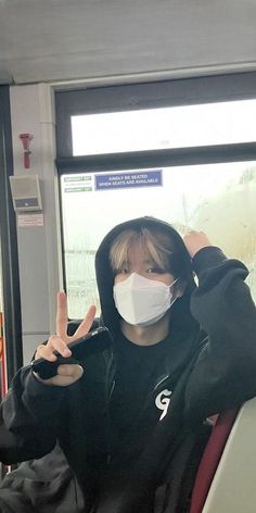 a person wearing a face mask sitting on a bus and making the peace sign with their hands