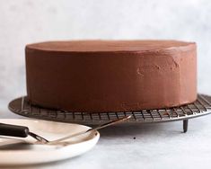 a chocolate cake sitting on top of a cooling rack next to a knife and fork