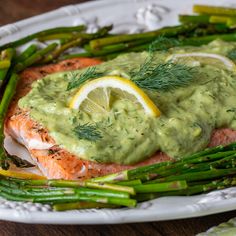 a white plate topped with salmon and asparagus covered in guacamole