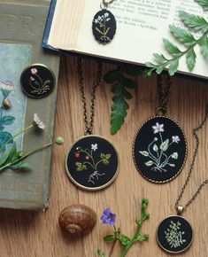 four embroidered pendants are sitting on a table next to an open book and flowers