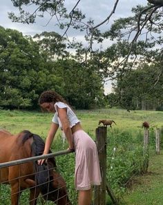 a woman standing next to a fence petting a horse