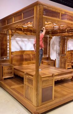 a man standing on top of a wooden bed frame in a room filled with furniture