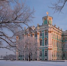 an ornate building with snow on the ground and trees in front of it at dusk