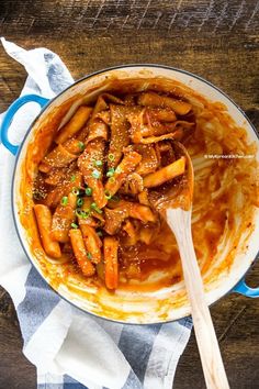 a pot filled with meat and noodles on top of a wooden table next to a spoon