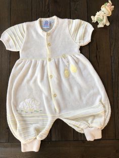 This adorable unisex romper is in excellent condition and appears to have never been worn. It is super soft to the touch and has an appliqué of little bears in white with embroidered yellow hearts and green and yellow and white checked balloons.  The roads company was started in the 60s in Venezuela and is still in operation. I am not able to precisely date this piece but according to the rodesbaby.com website they were in full manufacturing capacity by the 70s.  Size: 6 months  Materials: 100% acrylic Can be machine washed in cold water Cream Cotton Bubble Romper With Short Sleeves, Cream Short Sleeve Bubble Romper For Summer, Cute Cream Onesie For Spring, Cute Cream Onesie For Loungewear, White Onesie For Baptism In Spring, Fitted Cream Onesie For Summer, Spring Baptism Cotton Onesie, Summer Cream Cotton Onesie, Yellow Short Sleeve Onesie For Spring