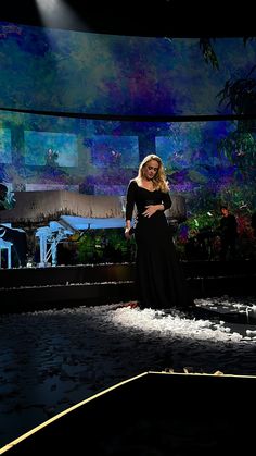 a woman in a black dress standing on stage with her hands on her hips and arms behind her back