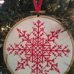 a cross stitch snowflake ornament hanging on a christmas tree with red ribbon