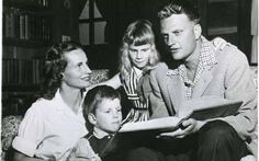 an old black and white photo of a man reading a book to two women and a boy