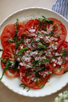 a white plate topped with sliced tomatoes and herbs