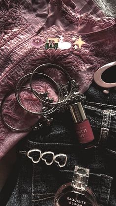 an open pair of jeans with rings and lipstick on it next to a bottle of perfume