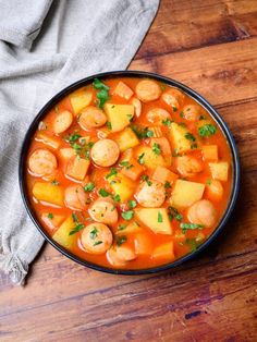 a bowl of stew with potatoes and carrots on a wooden table next to a gray napkin