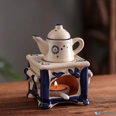 a ceramic teapot with a candle in it sitting on a wooden table next to a small stove