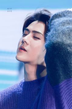 a man with his eyes closed wearing a purple sweater