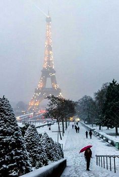 the eiffel tower is lit up with christmas lights in the snow and people are walking around