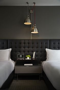 two white beds in a hotel room with black headboards and lamps above the bed