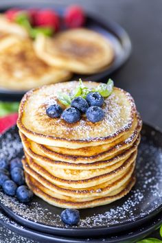 a stack of pancakes with blueberries and powdered sugar on top sitting on a plate